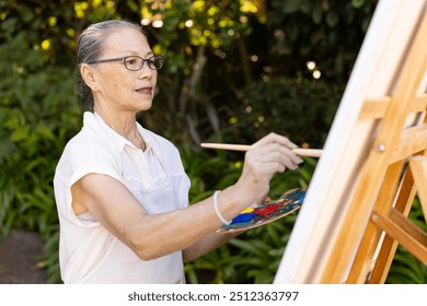 Painting on canvas, senior asian woman using brush and palette in outdoor setting. Art, creativity, nature, relaxation, hobby - Powered by Shutterstock