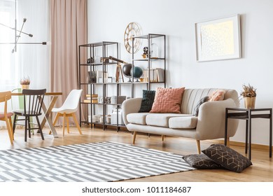 Painting on white wall above sofa with cushions in living room interior with chairs at the table under metal lamp - Shutterstock ID 1011184687
