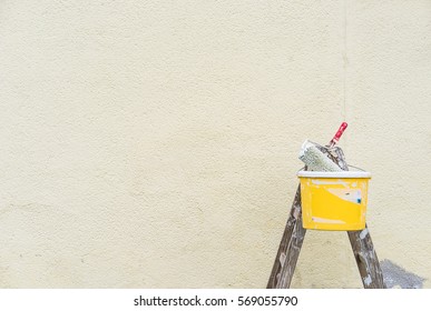 Painting outdoor walls with ladder, bucket and roller during renovation.
