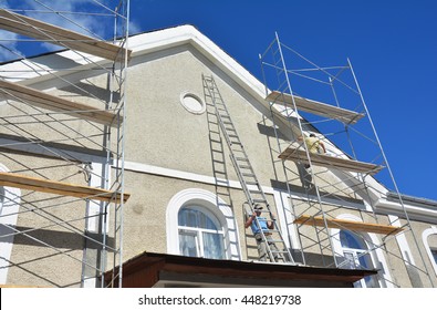 Painting and Plastering Exterior House Scaffolding Wall. Facade Thermal Insulation and Painting Works During Exterior Renovations. Builder Worker Plastering House Facade.