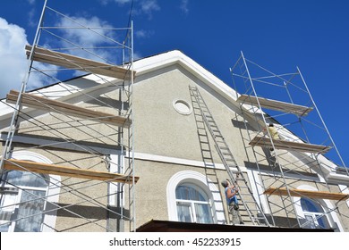 Painting and Plastering Exterior House Scaffolding Wall. Home Facade Insulation and Painting Works During Exterior Renovations. Builder Worker Plastering House Facade.