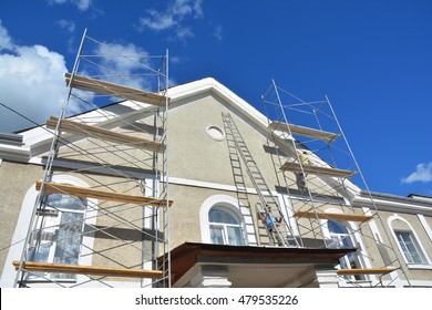 Painting And Plastering Exterior House Scaffolding Wall. Home Facade Insulation, Stucco And Painting Works During Exterior Wall  Renovations And Repair. Builder Worker Plastering House Facade Outdoor