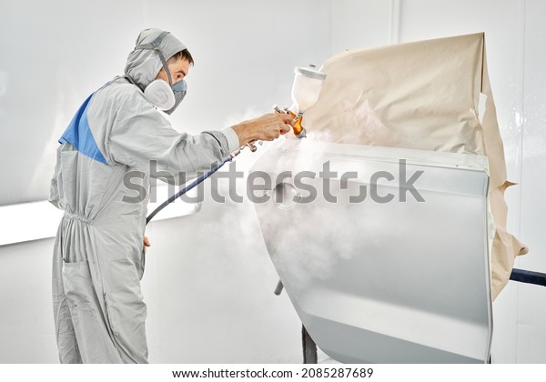 Painting the rear door of the\
car. Car painter in special painting chamber, wearing costume and\
protective gear. Car service station. Restoring a car after an\
accident