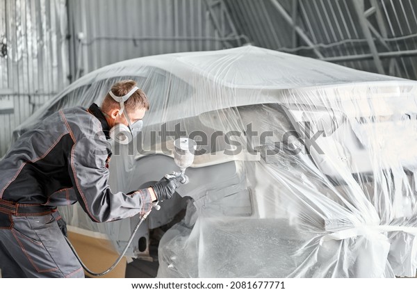 Painting the rear part of the car. Car painter\
wearing costume and protective gear. Car service station. Restoring\
a car after an\
accident