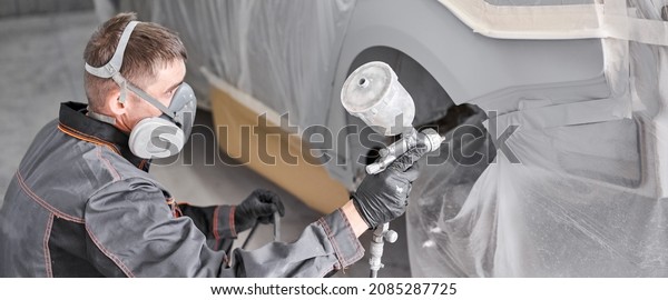 Painting the rear part of the car. Car painter\
wearing costume and protective gear. Car service station. Restoring\
a car after an\
accident