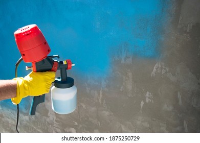 Painting A Roughly Plastered Wall With A Hand-held Spray Gun. Spray Gun Without Hose With Top Compressor. Copy Space For Text. Selective Focus. Household Repair, Construction.