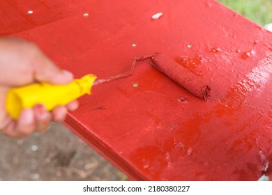 Painting The Seat Of An Old Glider Swing Made Of Wrought Iron With Red Oxide Primer Paint. Using A Small Paint Roller. Restoring Or Rebuilding Outdoor Furniture Or Playground Equipment.