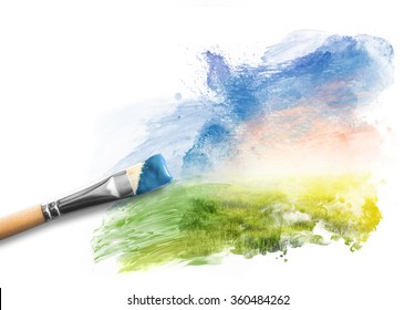Painting the spring landscape. Brush with blue paint over sky and green field. Concept of creating art, creativity, imagination.