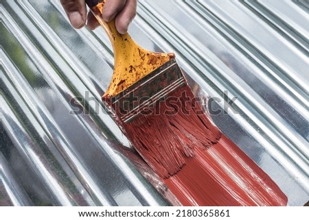 Painting the surface of a sheet of Galvanized Iron or GI corrugated metal with rust inhibiting red oxide primer.