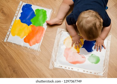 painting technology. gouache on the white paper in closed plastic bag, case or hood. one year age boy spreading paint by hands. home made art. children game. sensoric excersise.