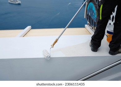 painting a white railing with a roller in Santorini