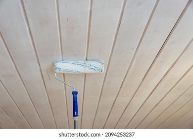 Painting the wooden ceiling with a roller and paint.