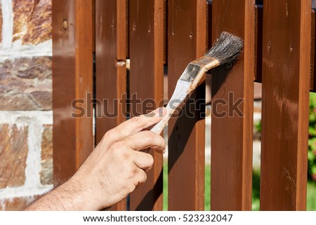 Painting wooden fence with a brown paint on a sunny day