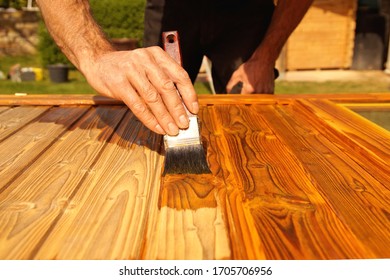 Painting woodwork outside in spring. Close-up of Male hand varnishes a door with a brush. Concept of renovation works, Carpentry details with woodwork and handyman. liquid wood preservative stain 