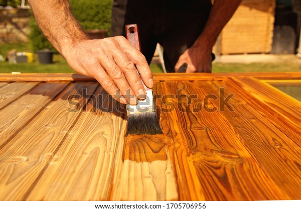 Painting woodwork outside in spring. Close-up of Male\
hand varnishes a door with a brush. Concept of renovation works,\
Carpentry details with woodwork and handyman. liquid wood\
preservative stain 
