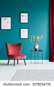 Paintings On The Green Wall In Living Room Interior With Red Armchair And Black Side Table With A Flower Vase On Top