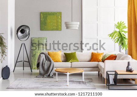 Paintings on the wall and industrial lamp in the corner of elegant living room interior with golden lime accents, real photo with copy space