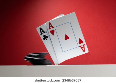 A pair of aces are balancing over the table, next to a stack of poker chips.  On a red background, copy space
