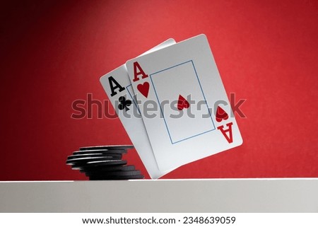 A pair of aces are balancing over the table, next to a stack of poker chips.  On a red background, copy space