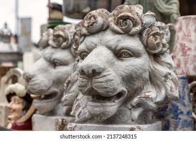 A pair of antique decorative lion head plant pots, with roses forming the mane. Other antiques and bric-a-brac can be seen in the background of a market stall. - Shutterstock ID 2137248315