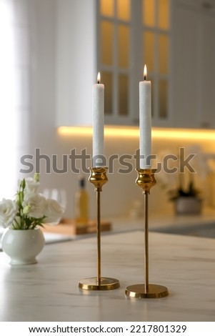 Pair of beautiful golden candlesticks on white marble table in kitchen