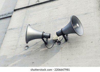 Pair of big retro loudspeakers mounted on grey concrete cement wall. Air raid nuclear strike alert speaker siren. Urgent or emergency announcement, message event. Dictatorship regime concept