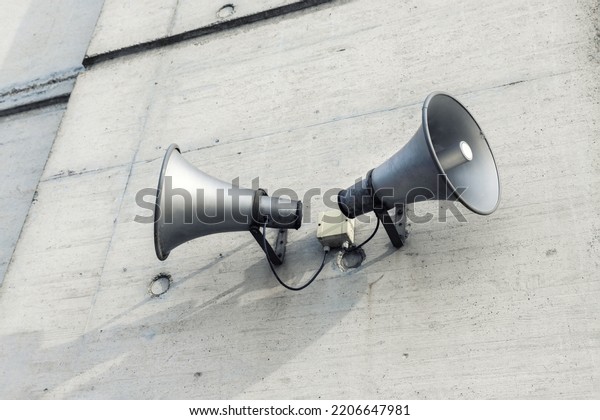 Pair of big retro loudspeakers mounted on grey\
concrete cement wall. Air raid nuclear strike alert speaker siren.\
Urgent or emergency announcement, message event. Dictatorship\
regime concept