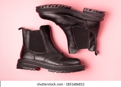 A pair of black autumn boots on a pink background, view from above