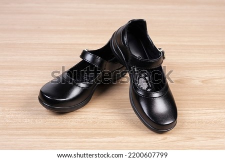 A pair of black female student shoes on wood floor.