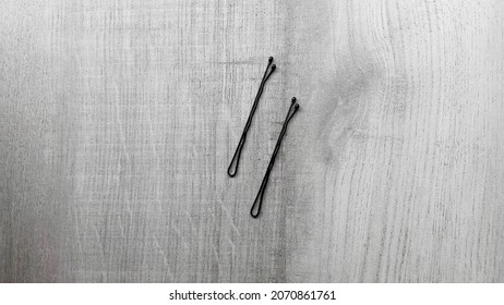 A pair of black hairpins isolated on a gray wooden table.                    