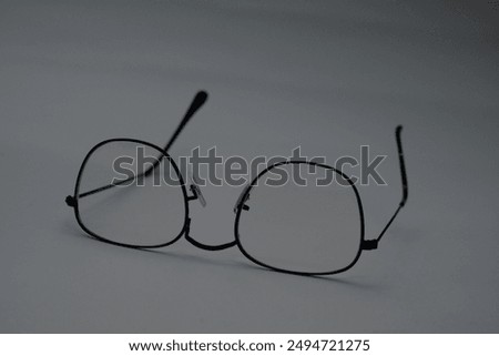 A pair of black, rectangular glasses with clear lenses rests on a gray surface. The glasses are slightly askew, suggesting a sense of disorientation or neglect.