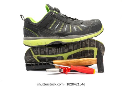 Pair of black safety shoes with green lining along with a hammer with wooden handle, a red pliers and a red Phillips screwdriver. With a white background.