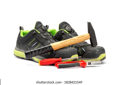 Pair of black safety shoes with green lining along with a hammer with wooden handle, a red pliers and a red Phillips screwdriver. With a white background.