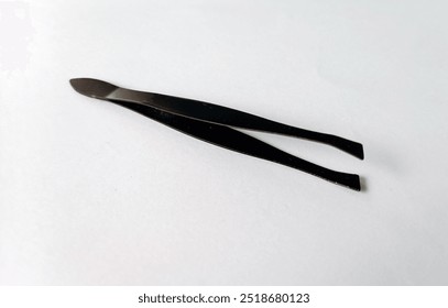 A pair of black tweezers lying on a white surface, commonly used for precision tasks and grooming - Powered by Shutterstock