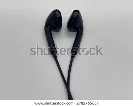 A pair of black wired earbuds placed on a plain gray surface, showcasing a sleek and minimalistic design.

