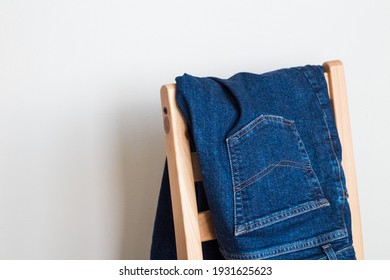 Pair of blue jeans folded on a wooden chair, white background