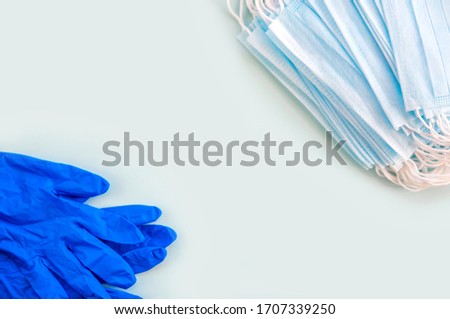 A pair of blue latex medical gloves and an earloop surgical mask on a blue background. Protection concept