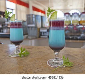 Pair of blue ornate cocktail drinks with lemon and mint on marble bar counter top