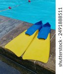 a pair of blue and yellow coloured flippers on the side of a clear water swimming pool. Sports accessories for swimming. 