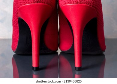 A Pair Of Bright Red Stiletto Heel Boots With Black Soles, Close-up Of Back View, On A Gray Background And Reflected In A Shiny Surface.