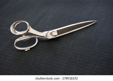 Pair Of Bright Shiny Silver Steel Fabric Shears Or Designer Scissors For Cutting Material Lying On A Grey Textile With Copyspace