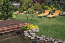 A Pair Of Bright Yellow Designer Lawn Chairs Invite You To Relax In This Beautifully Landscaped Backyard With Deck Spanning A Creek In The Foreground.