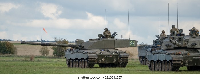 A Pair Of British Army Challenger II 2 FV4034 Main Battle Tanks In Action Crossing Open Grass Fields, On A Military Exercise Wiltshire UK