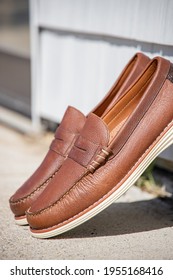 A Pair Of Brown Leather Loafers For Men Against A Modern Wooden Wall In The Sun For An Outdoor Fashion Photoshoot Of Footwear.