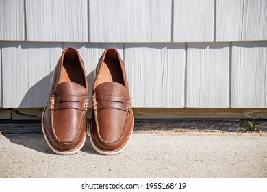 A Pair Of Brown Leather Loafers For Men Against A Modern Wooden Wall In The Sun For An Outdoor Fashion Photoshoot Of Footwear.