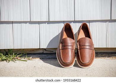 A Pair Of Brown Leather Loafers For Men Against A Modern Wooden Wall In The Sun For An Outdoor Fashion Photoshoot Of Footwear.