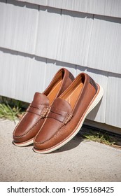 A Pair Of Brown Leather Loafers For Men Against A Modern Wooden Wall In The Sun For An Outdoor Fashion Photoshoot Of Footwear.