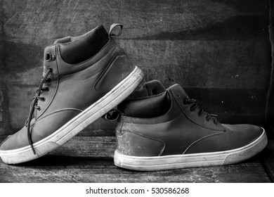 A pair of brown shoes with leather trim and untied laces, in black and white on a wooden table against a wooden background. - Powered by Shutterstock