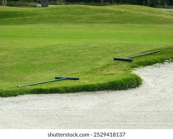 Pair of bunker rakes placed by a recently raked fairway bunker on a municipal golf course in southwest Florida, for motifs of maintenance, consistency, and etiquette - Powered by Shutterstock