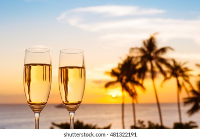 Pair of champagne glasses against a beautiful tropical sunset.  